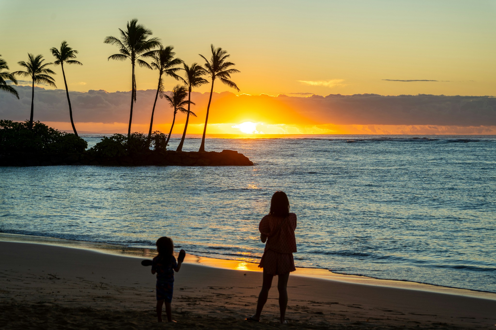 Strand bei Honolulu mit Palmen und Sonnenuntergang über dem Meer