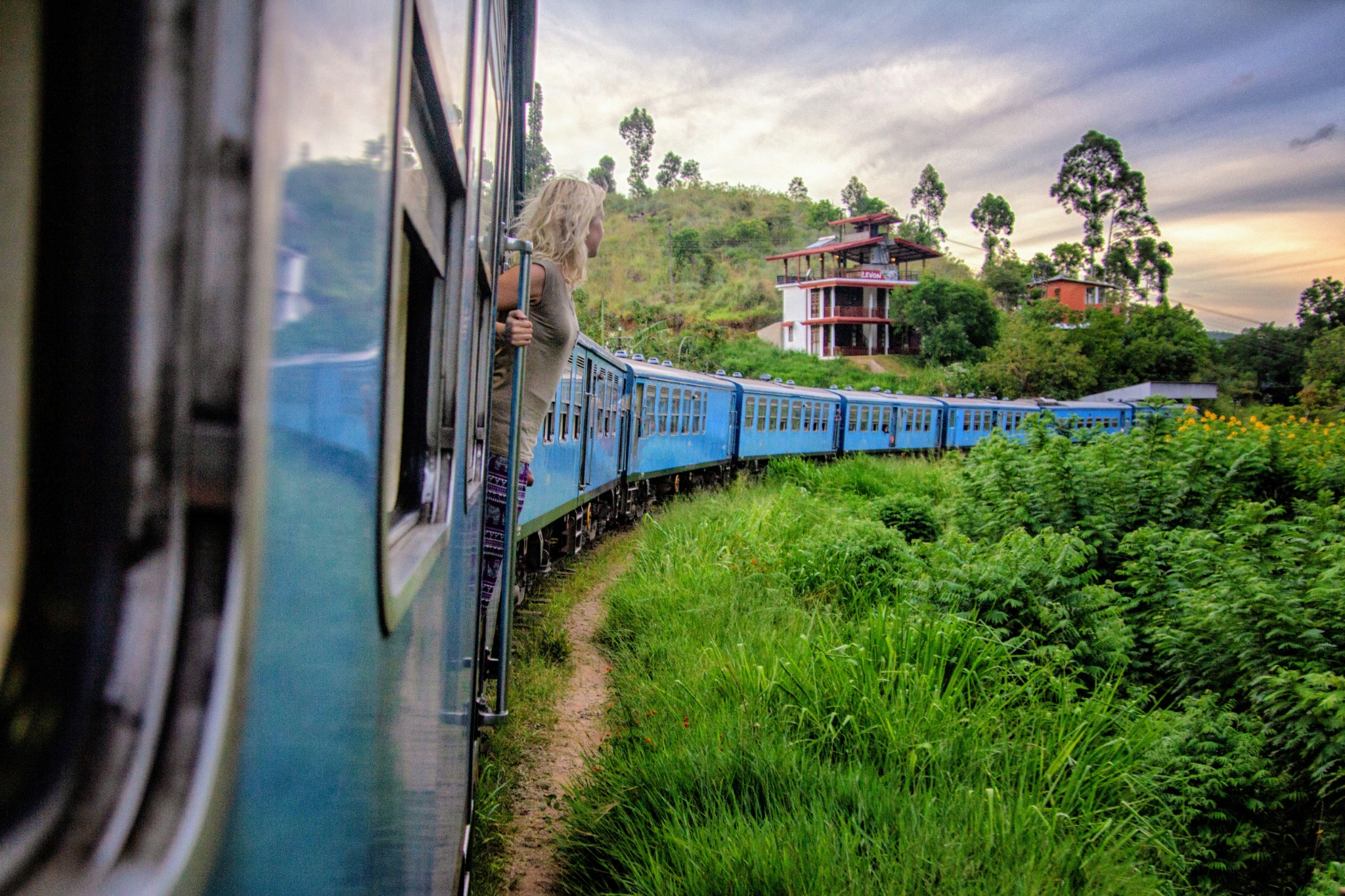 Blauer Zug fährt durch eine grüne Hügellandschaft in Sri Lanka.